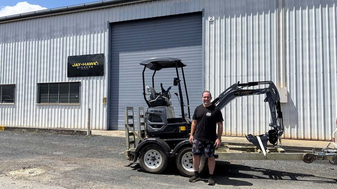 Glen with his new JHM14K mini excavator loaded on a trailer outside the Jay-Hawk Diggers sign