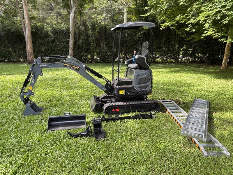 Jay-Hawk JHM14 on grass with the full attachment bundle laid out — buckets, ramps, hitch