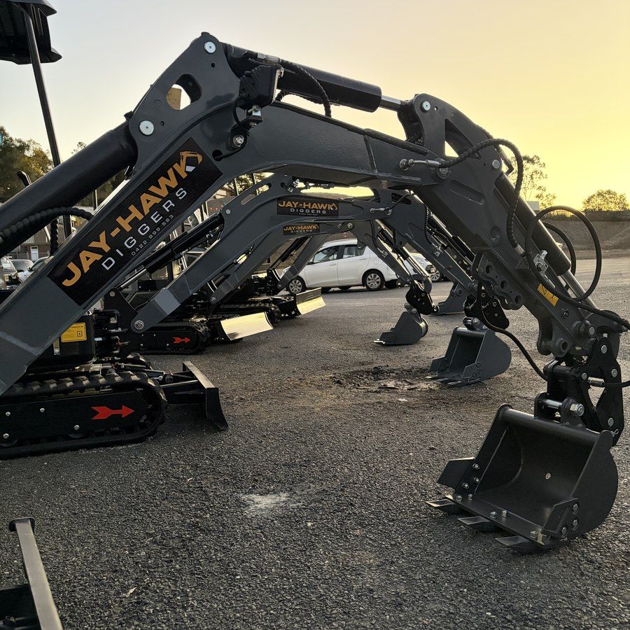 Close-up of a Jay-Hawk excavator boom and bucket, branded arm decal, sunset light